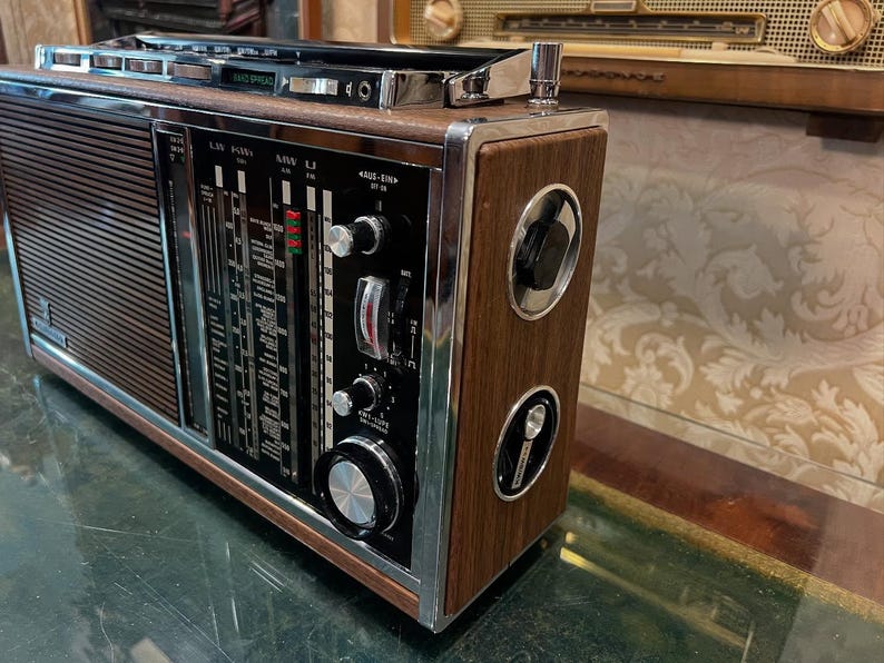 May include: A vintage radio with a wood grain finish and chrome accents. The radio features a tuning dial, various knobs, and a speaker grill. The face of the radio has a black panel with white and red markings. The radio is a retro style.