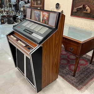 May include: A vintage wooden jukebox with a black front panel and a glass display. The jukebox has a selection of buttons and a record player. The jukebox is labeled "MOD-K STEREO".
