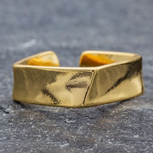 Op de afbeelding: Een ring van goudkleurig metaal met een vierkante vorm en een licht getextureerd oppervlak.