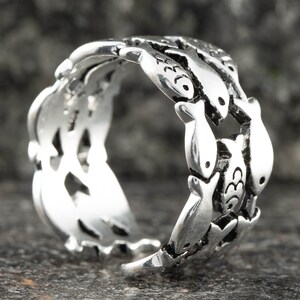 May include: A silver ring featuring a repeating pattern of fish. The ring has a detailed design with each fish individually crafted. The ring is made of a shiny, metallic material and is set against a dark background.