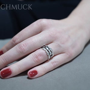 May include: A silver ring with a repeating leaf design, set with small clear stones. The ring is worn on a finger with red nail polish. The brand name "ABASCHMUCK" is visible in the background.