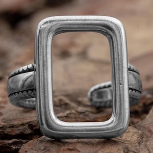 Könnte beinhalten: Ein silberner Ring mit einem rechteckigen, offenen Design. Der Ring hat eine strukturierte Band.