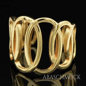 May include: A gold-colored ring with an interwoven design of oval shapes. The ring has a polished finish and is set against a black background. The brand name "ABASCHMUCK" is visible at the bottom.
