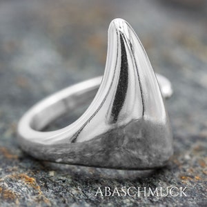 May include: A silver ring with a unique, angular design. The ring is shaped like a sharp, pointed triangle.