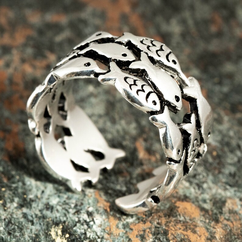 May include: A silver-colored ring featuring a design of small fish swimming around the band. The ring has an open design, allowing for some adjustment in size. The fish are detailed with etched features, creating a unique aquatic theme.