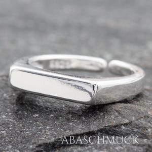 Könnte beinhalten: Ein silberner Ring mit einem rechteckigen Band. Der Ring ist schlicht und minimalistisch im Design.