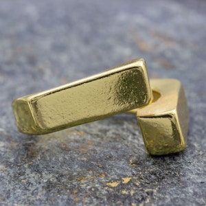 Könnte beinhalten: Zwei goldfarbene Metallringe, einer ist ein einfaches Rechteck und der andere ein gebogenes Rechteck, liegen übereinander.