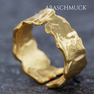 Könnte beinhalten: Ein goldener Ring mit einer strukturierten, unregelmäßigen Oberfläche. Der Ring ist dick und hat eine breite Band.