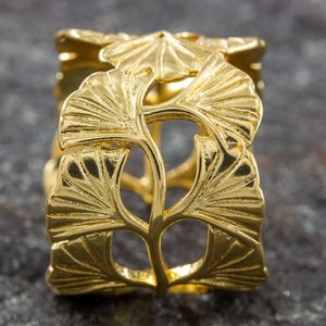 Könnte beinhalten: Serviettenring aus goldfarbenem Metall mit einem detaillierten Design aus Ginkgoblättern.