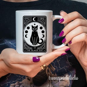 May include: White ceramic mug with a black and white illustration of a black cat with a crescent moon and stars. The text "The Black Cat" is printed on the mug.