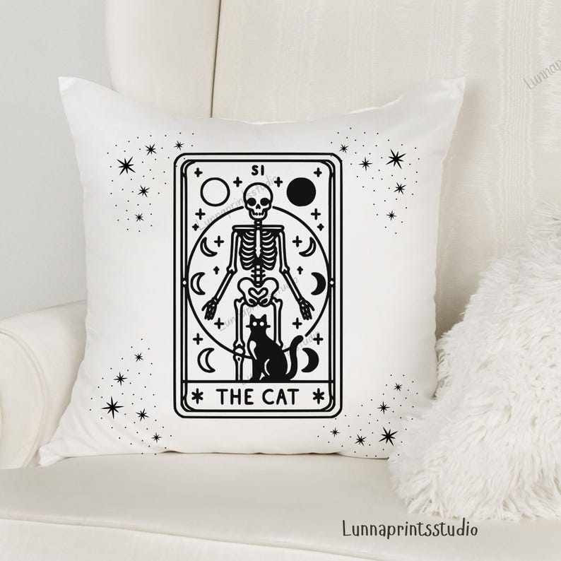 May include: White throw pillow with a black and white illustration of a tarot card depicting a skeleton holding a cat. The card reads "The Cat" and is surrounded by stars.