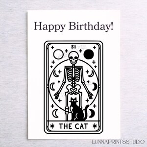 May include: Black and white illustration of a tarot card with a skeleton and a black cat. The card is titled "The Cat".