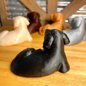 May include: A collection of five small, 3D printed dachshund figurines in various colors, including black, brown, white, and gray. The figurines are posed in a sitting or lying down position.