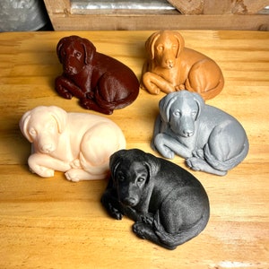 May include: Five ceramic dog figurines in different colors, including brown, beige, gray, and black. The dogs are all in a lying down position with their heads resting on their paws.