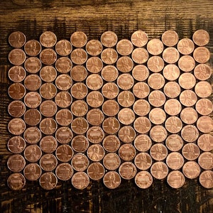 May include: A large collection of copper-colored US pennies arranged in a wave pattern on a wooden surface.