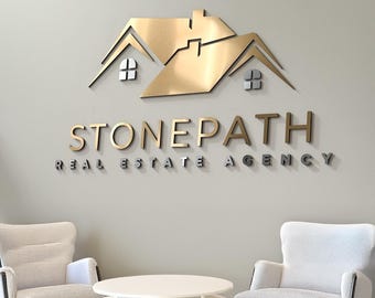 May include: A wall-mounted sign for Stonepath Real Estate Agency, featuring a gold-colored house silhouette above the company name. The text "REAL ESTATE AGENCY" is below the name. Two white armchairs and a round table are in the foreground.