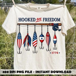 Może przedstawiać: Kremowy t-shirt z krótkim rękawem z grafiką wędki i sześcioma wiszącymi przynętami. Napis głosi HOOKED on FREEDOM oraz 1776. Przynęty ozdobione są czerwono-biało-niebieskimi wzorami, w tym motywami gwiazd i pasów.