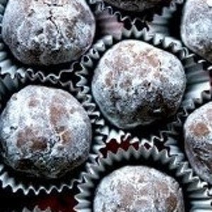 May include: Close-up of a group of chocolate truffles dusted with powdered sugar, arranged in paper baking cups.