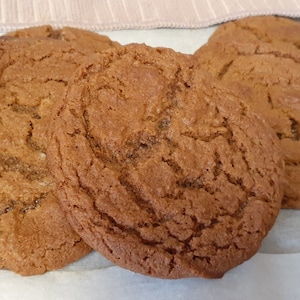 May include: Three brown gingerbread cookies on a white parchment paper background.