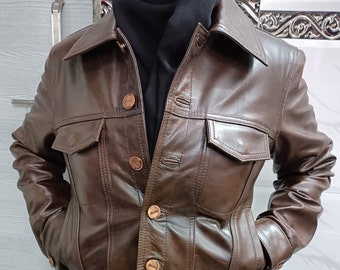 May include: A brown leather jacket with a denim-style design. The jacket has a collared neckline, long sleeves, and multiple pockets. The jacket features copper-colored buttons.