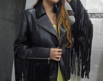Puede incluir: Chaqueta de cuero negra con largos detalles de flecos en las mangas y el dobladillo. La chaqueta tiene cierre de cremallera y cuello alto.
