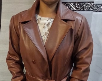 May include: A brown leather trench coat with a double-breasted closure, a belt, and long sleeves.