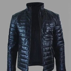 Puede incluir: Una chaqueta de cuero acolchada negra con cierre de cremallera. La chaqueta tiene un cuello alzado y una silueta ligeramente ajustada.