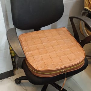 Peut inclure: Un fauteuil de bureau noir avec un coussin de siège en cuir marron. Le coussin a une fermeture éclair et un design matelassé.