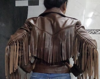 Könnte beinhalten: Braune Lederjacke mit langen Fransen an den Ärmeln und am Rücken. Die Jacke hat ein kurzes Design und einen klassischen Kragen. Das Model trägt eine blaue Jeans. Die Jacke hat eine mittelbraune Farbe.