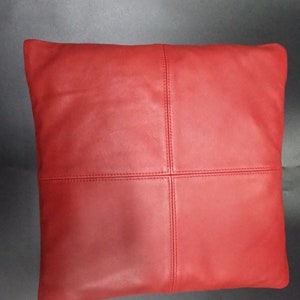 May include: Red leather pillow with a square design. The pillow is made of four panels of leather that are stitched together.