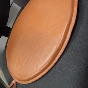May include: A round brown leather chair cushion with a stitched edge.