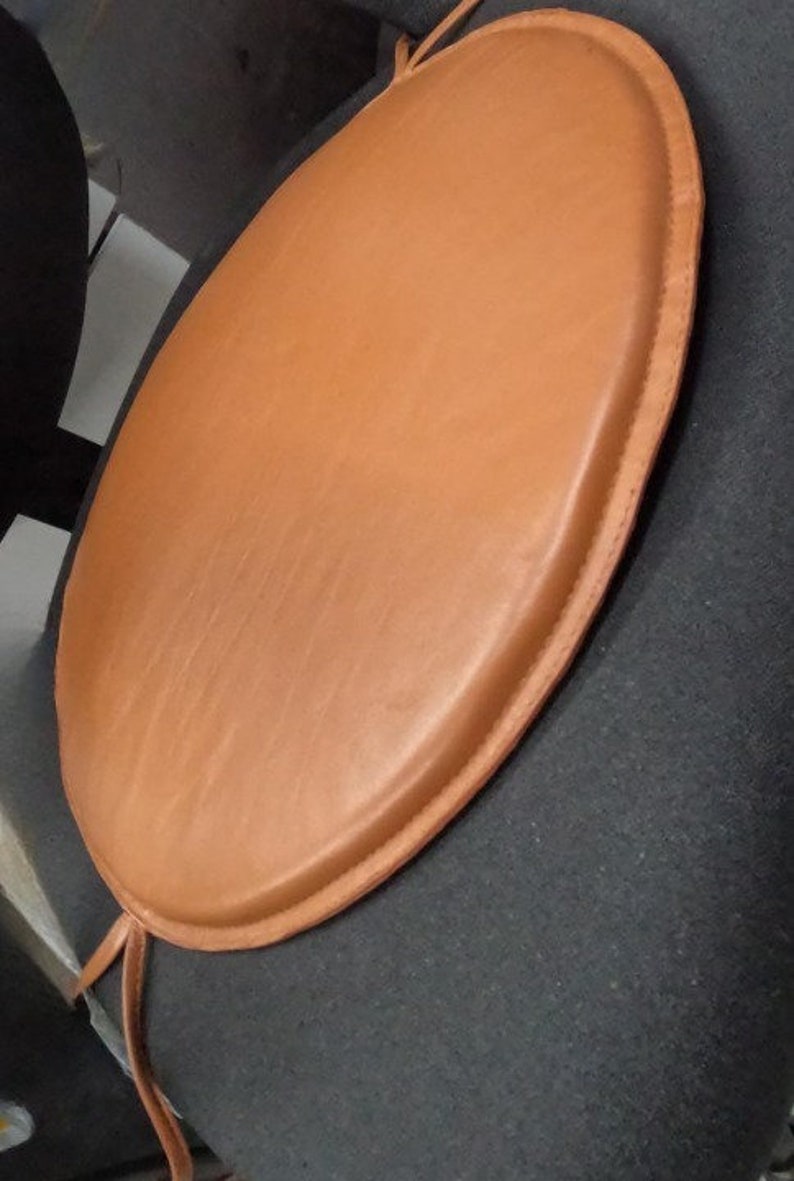 May include: A round brown leather chair cushion with a stitched edge.