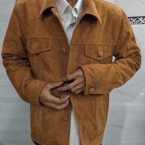 May include: A brown suede jacket with a button-up front and two flap pockets. The jacket has a collar and long sleeves.