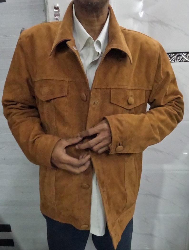 May include: A brown suede jacket with a button-up front and two flap pockets. The jacket has a collar and long sleeves.