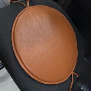 May include: A round brown leather chair cushion with a tied string.