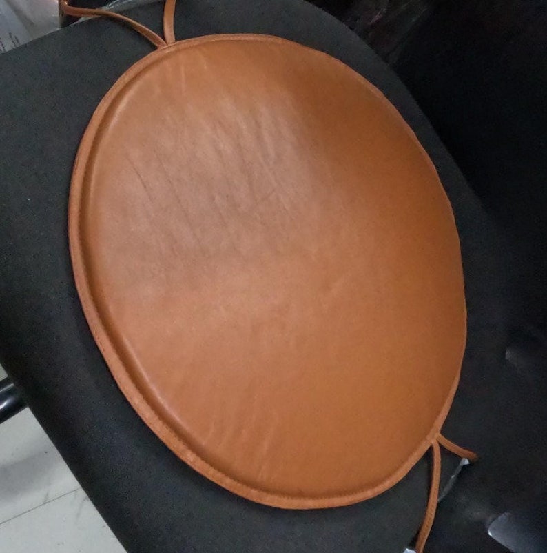 May include: A round brown leather chair cushion with a tied string.