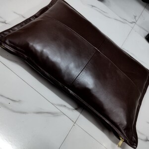 May include: A brown leather cushion with a zipper closure. The cushion is rectangular in shape and made from soft, supple leather.