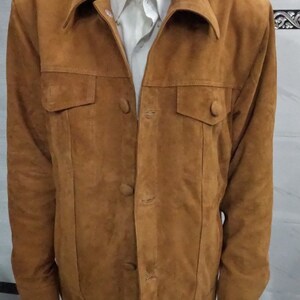 May include: A brown suede jacket with a button-up front and two flap pockets. The jacket has a collar and long sleeves.