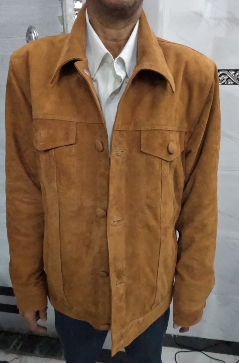 May include: A brown suede jacket with a button-up front and two flap pockets. The jacket has a collar and long sleeves.