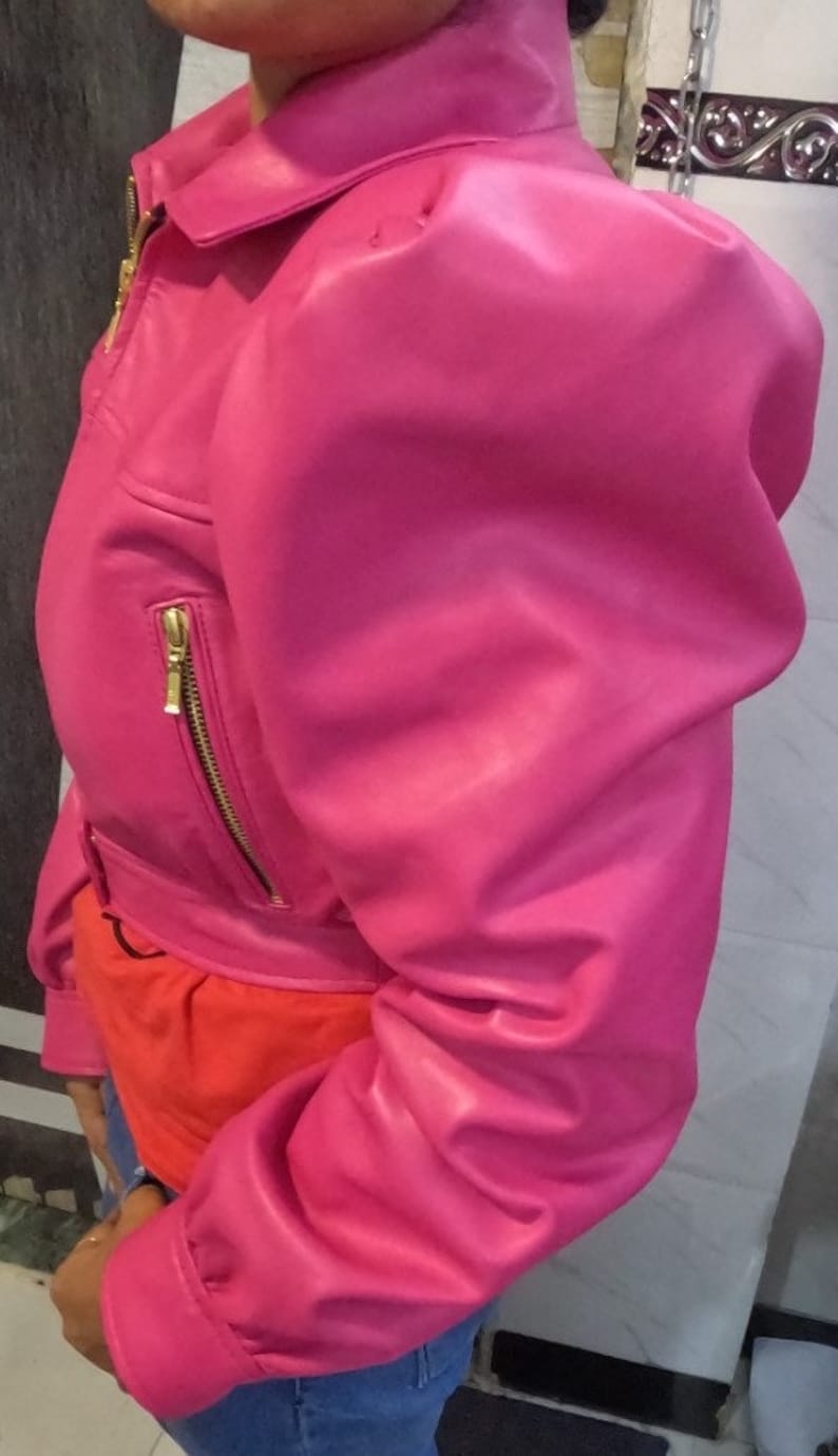 May include: A pink leather jacket with a cropped style and puffed sleeves. The jacket has a zipper closure and gold hardware.