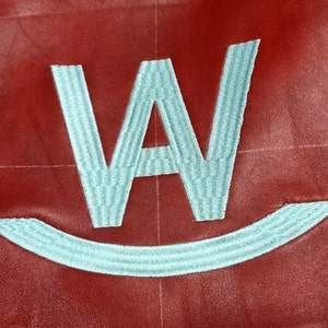 Puede incluir: Una "W" bordada en blanco con una sonrisa debajo sobre un fondo rojo.