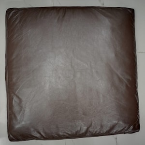 May include: A brown leather cushion with a slightly textured surface.