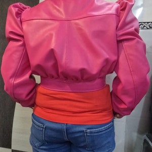May include: A cropped pink leather jacket with puffed sleeves. The jacket has a zipper closure and a collar.