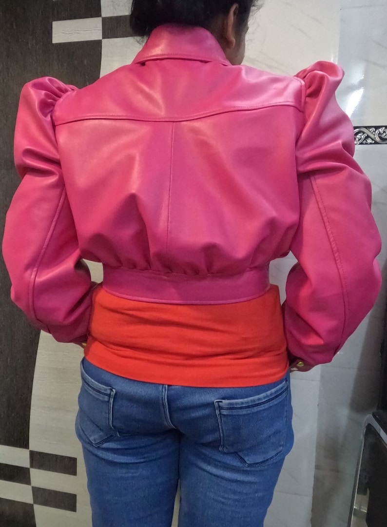 May include: A cropped pink leather jacket with puffed sleeves. The jacket has a zipper closure and a collar.