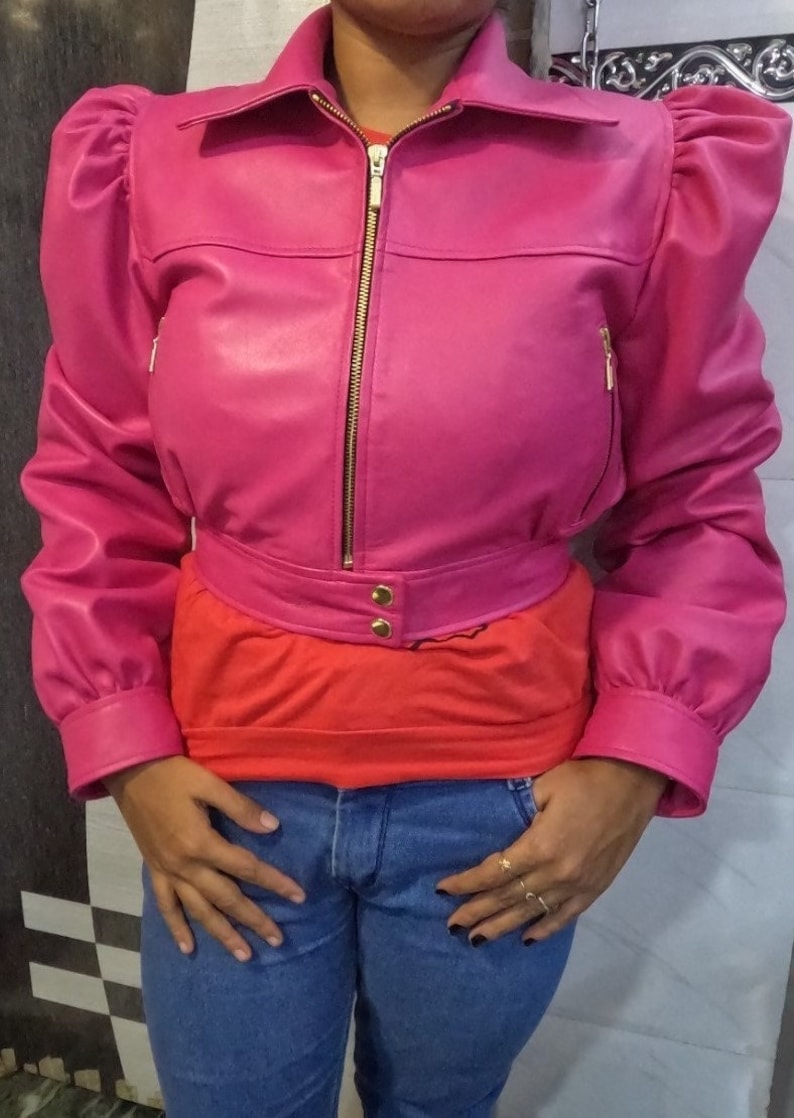 May include: A cropped pink leather jacket with a zipper closure and puffed sleeves. The jacket has a gold zipper and buttons.