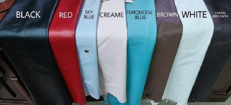 May include: A close-up of eight different coloured leather swatches. The swatches are arranged from left to right: black, red, sky blue, cream, turquoise blue, brown, white, and dark brown.