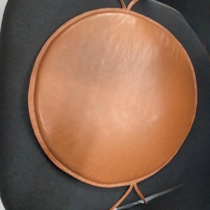 May include: A round brown leather chair cushion with a tie closure.