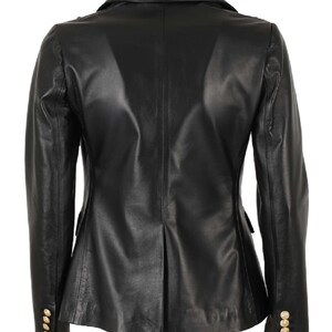 K&ouml;nnte beinhalten: Ein schwarzer Lederblazer mit doppelreihigem Verschluss und goldenen Kn&ouml;pfen. Der Blazer hat einen Schalkragen und lange &Auml;rmel.