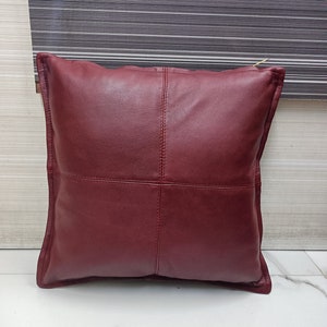 May include: A burgundy leather pillow with a square design. The pillow has a zipper closure and is made of soft, supple leather.