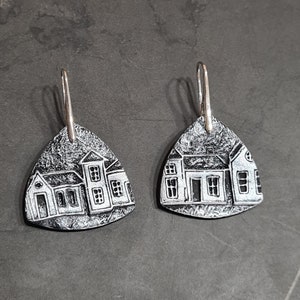Puede incluir: Un par de pendientes de plata con una imagen en blanco y negro de un pueblo pequeño en cada pendiente.